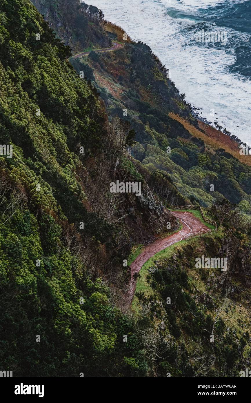Un tortuoso sentiero di terra rossa traccia le ripide scogliere di Faja sull'isola di Sao Jorge, offrendo vedute dell'oceano e mostrando il paesaggio vulcanico e lussureggiante di Th Foto Stock