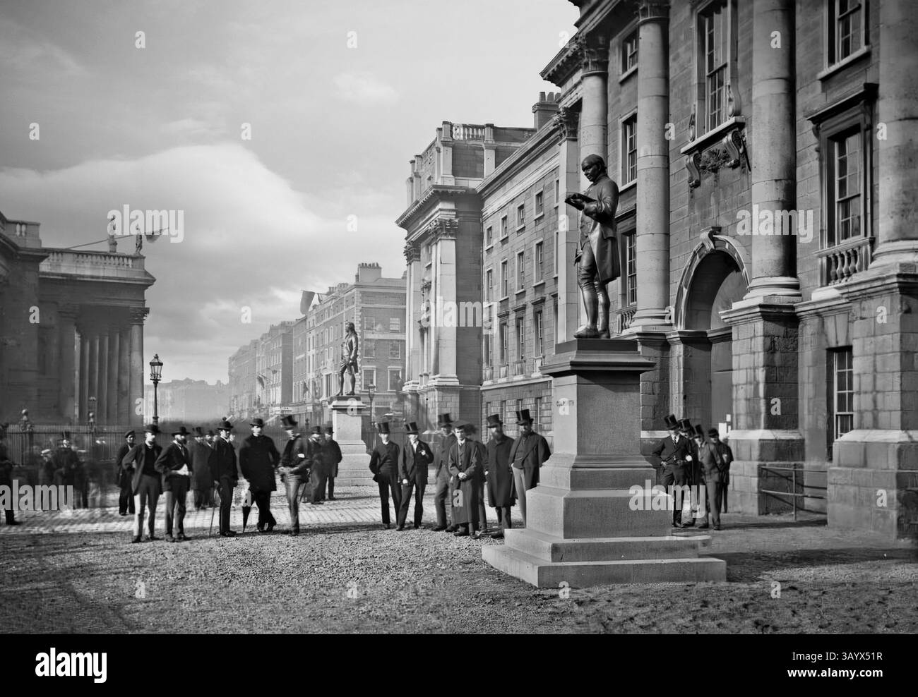 Una veduta della fine del XIX secolo di gentiluomini dall'alto si riunì intorno alla statua di Goldsmith all'ingresso della Regent House, che funge da ingresso centrale al campus del Trinity College di Dublino, Irlanda. Il «Front Gate» (ingresso della Regent House) dei terreni del college è stato costruito negli anni '1750 e conduce dal College Green, con una grande porta in legno con una porta più piccola e di dimensioni normali scolpita nel mezzo, che incanala i pedoni nell'edificio. Foto Stock