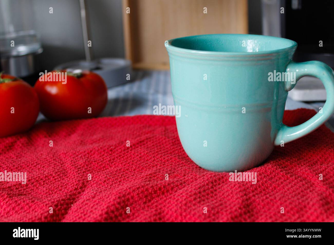 Cucina colorata con tazza da caffè turchese, telo da tè rosso e pomodori. Foto Stock