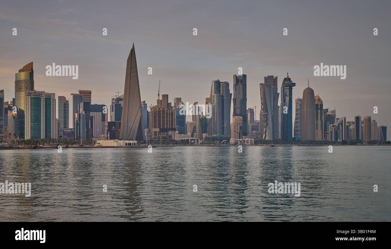 Skyline di Doha in Qatar dal tramonto sul lungomare di Corniche che mostra i dhows nel golfo arabo con la bandiera del Qatar Foto Stock