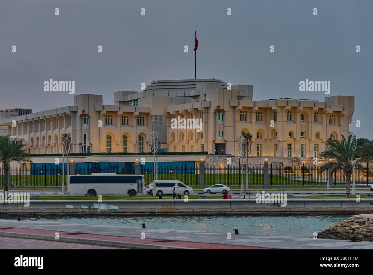 L'Amiri Diwan a Doha, Qatar, dal lungomare di Corniche, fotografato al tramonto con la bandiera del Qatar e le auto in strada Foto Stock