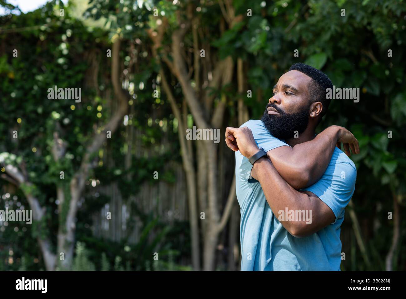 Uomo afro-americano che tira il braccio sul petto nel cortile posteriore, con smartwatch, spazio copia Foto Stock