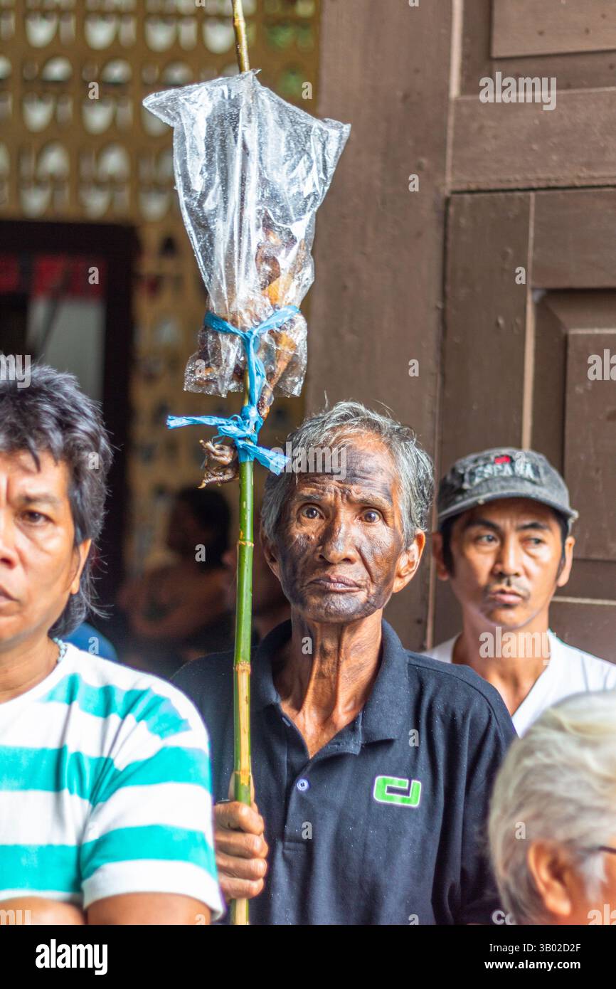 Un vecchio con il volto dipinto di nero tiene la carne alla griglia durante il Festival Ibajay ATI-ATI di Aklan, una vivace celebrazione in onore dello sto Niño Foto Stock