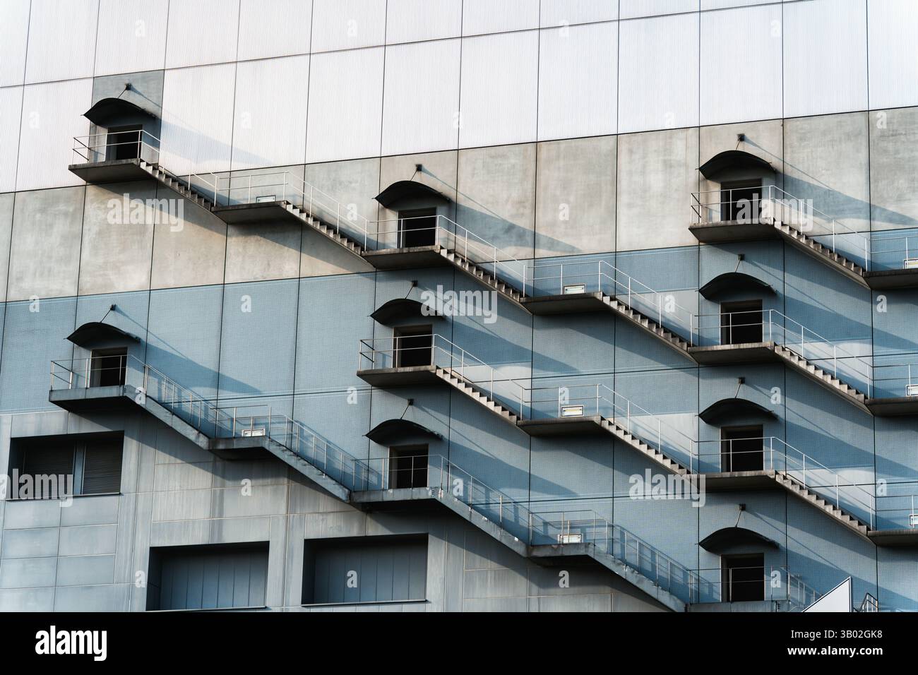 Edificio moderno con scale antincendio ripetute che proiettano un'ombra ritmica nella luce Foto Stock