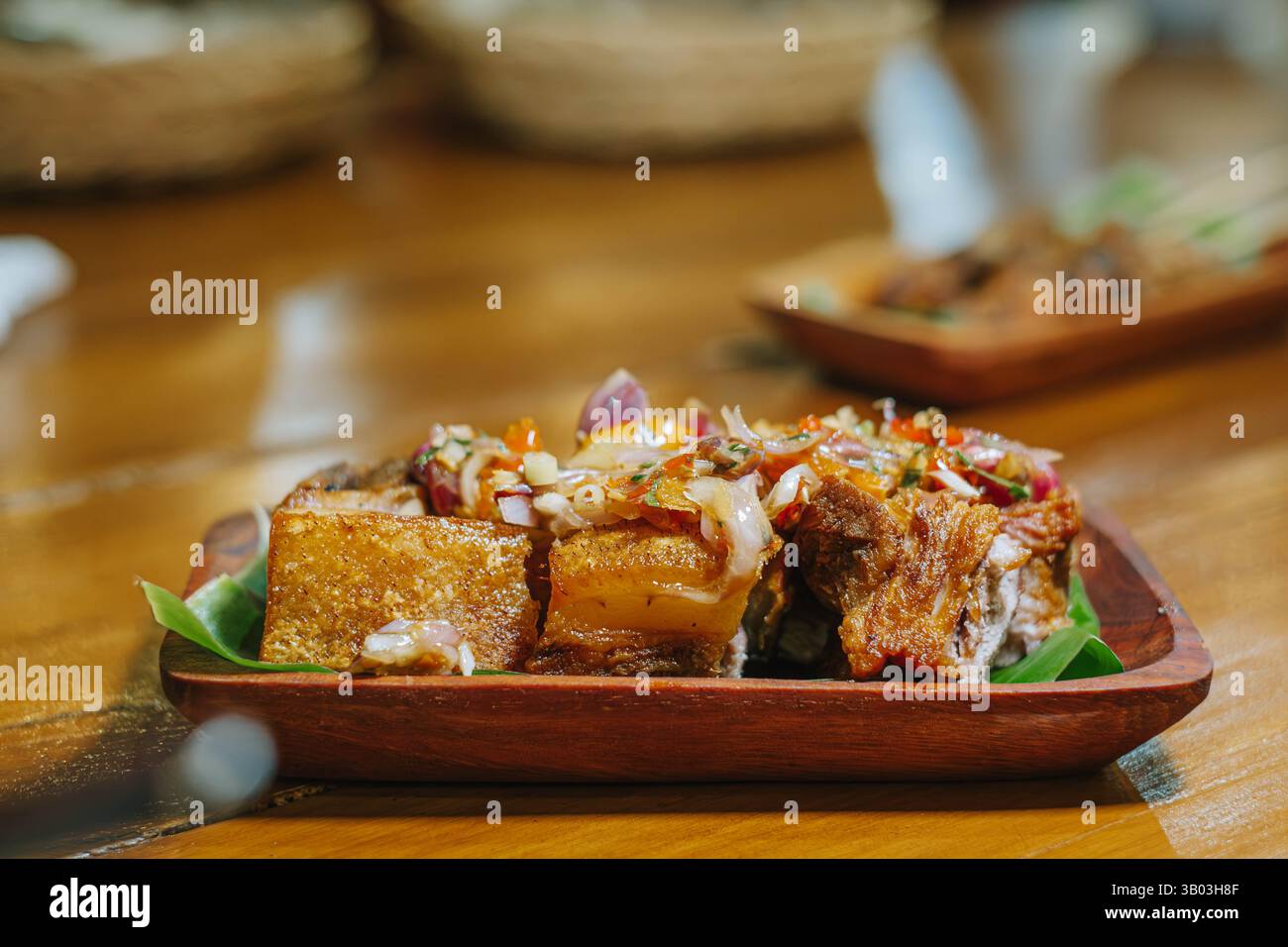 Pancetta di maiale croccante fritta con matah sambal su un piatto di legno con sfondo bokeh. Cucina tradizionale balinese. Foto Stock