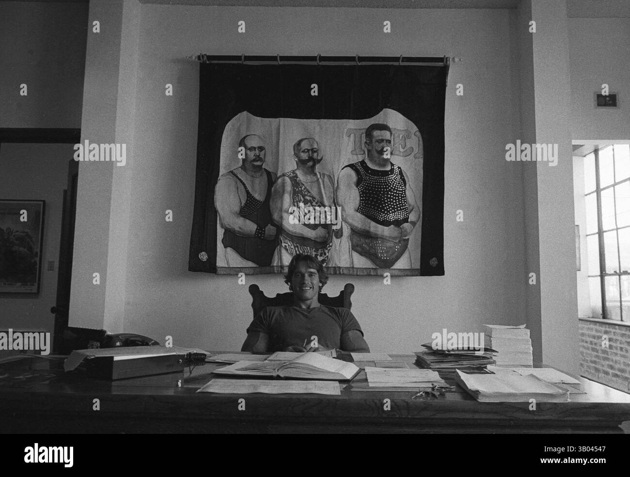 29 marzo 1979; Los Angeles, CA, Stati Uniti; il bodybuilder professionista ARNOLD SCHWARZENEGGER siede alla sua scrivania di fronte a un arazzo raffigurante uomini muscolari. Nato in un piccolo villaggio in Austria, Arnold iniziò ad allenarsi con i pesi in giovane età e presto raggiunse la vetta come campione di bodybuilding. La sua pausa nella recitazione è arrivata nel film di successo del 1982 "Conan the Barbarian". Da Conan, Arnold ha mantenuto una lunga carriera come attore. Arnold divenne anche attivo nella politica degli Stati Uniti all'inizio degli anni '80 e da allora è stato votato come governatore della California attraverso un controverso richiamo dell'ex governatore G. Foto Stock