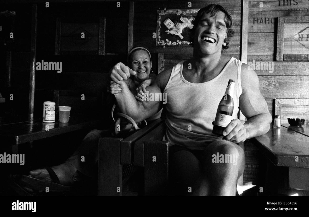 12 luglio 1979; Los Angeles, CA, Stati Uniti; il bodybuilder professionista ARNOLD SCHWARZENEGGER si flette per la macchina fotografica e un amico mentre beve una birra con lei. Nato in un piccolo villaggio in Austria, Arnold iniziò ad allenarsi con i pesi in giovane età e presto raggiunse la vetta come campione di bodybuilding. La sua pausa nella recitazione è arrivata nel film di successo del 1982 "Conan the Barbarian". Da Conan, Arnold ha mantenuto una lunga carriera come attore. Arnold è stato attivo nella politica degli Stati Uniti a partire dai primi anni '80 e da allora è stato votato come governatore della California a causa di un controverso richiamo dell'ex G Foto Stock