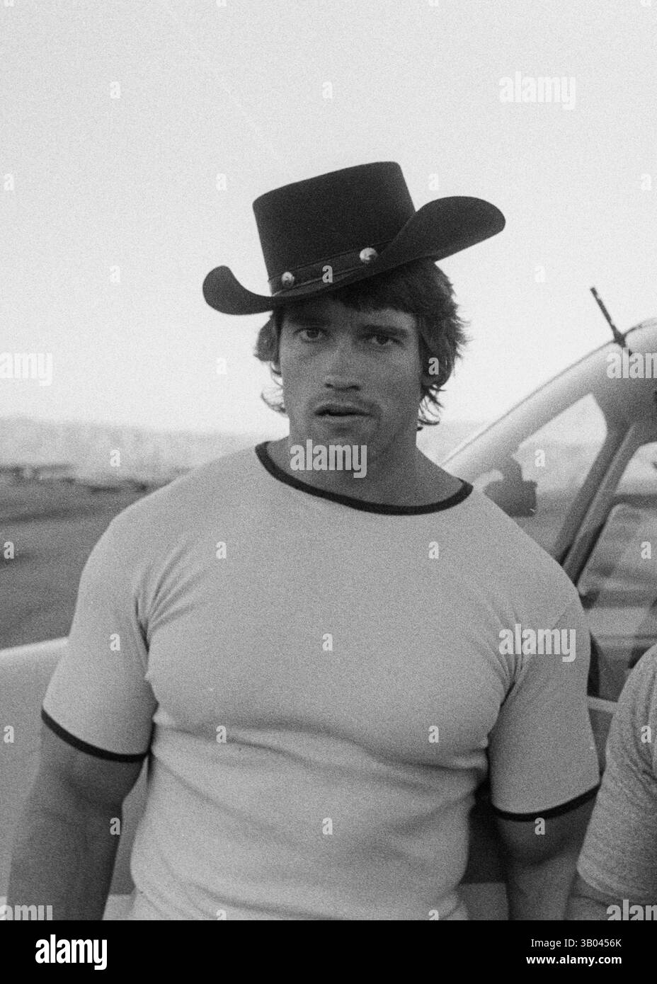 27 luglio 1979; Los Angeles, CA, Stati Uniti; il bodybuilder professionista ARNOLD SCHWARZENEGGER indossa un cappello da cowboy su una pista ventosa di fronte a dove è parcheggiato il suo piccolo aereo. Nato in un piccolo villaggio in Austria, Arnold iniziò ad allenarsi con i pesi in giovane età e presto raggiunse la vetta come campione di bodybuilding. La sua pausa nella recitazione è arrivata nel film di successo del 1982 "Conan the Barbarian". Da Conan, Arnold ha mantenuto una lunga carriera come attore. Arnold è stato attivo nella politica degli Stati Uniti a partire dai primi anni '80 e da allora è stato eletto governatore della California Foto Stock