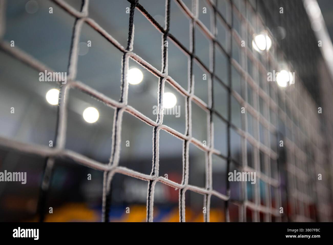 Primo piano di una rete da pallavolo nera quadrata con sfondo sfocato che mostra forme colorate indistinte e luci accese in un pallavolo interno Foto Stock