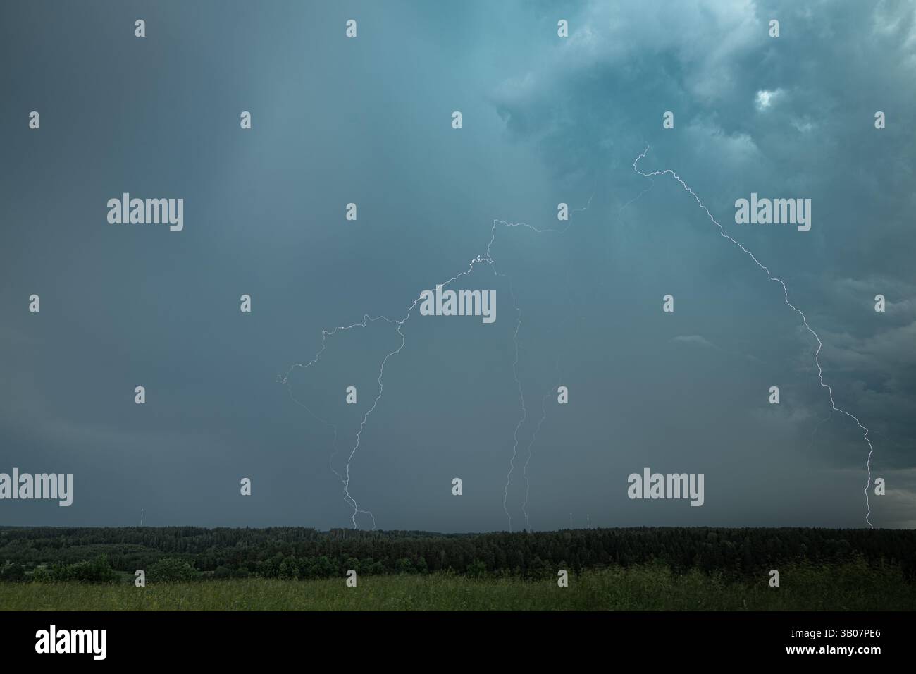 Fulmini vivi attraversano un cielo scuro durante un temporale estivo, elettrificando l'orizzonte sopra una fitta foresta. Foto Stock