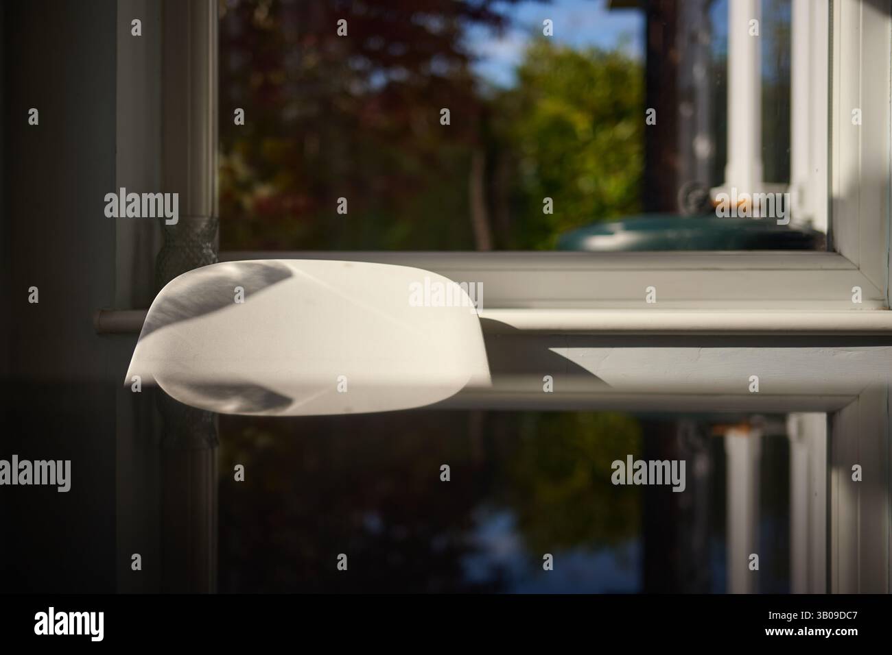 Sole basso su un tavolo da cucina e una sedia davanti a una finestra che si affaccia su un giardino Foto Stock