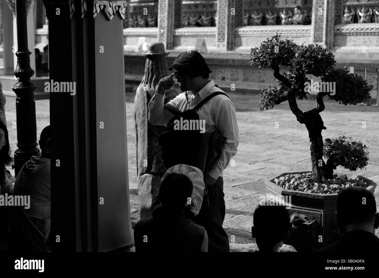 Una guida turistica condivide le storie con i visitatori in un corridoio ombreggiato del Grand Palace di Bangkok Foto Stock