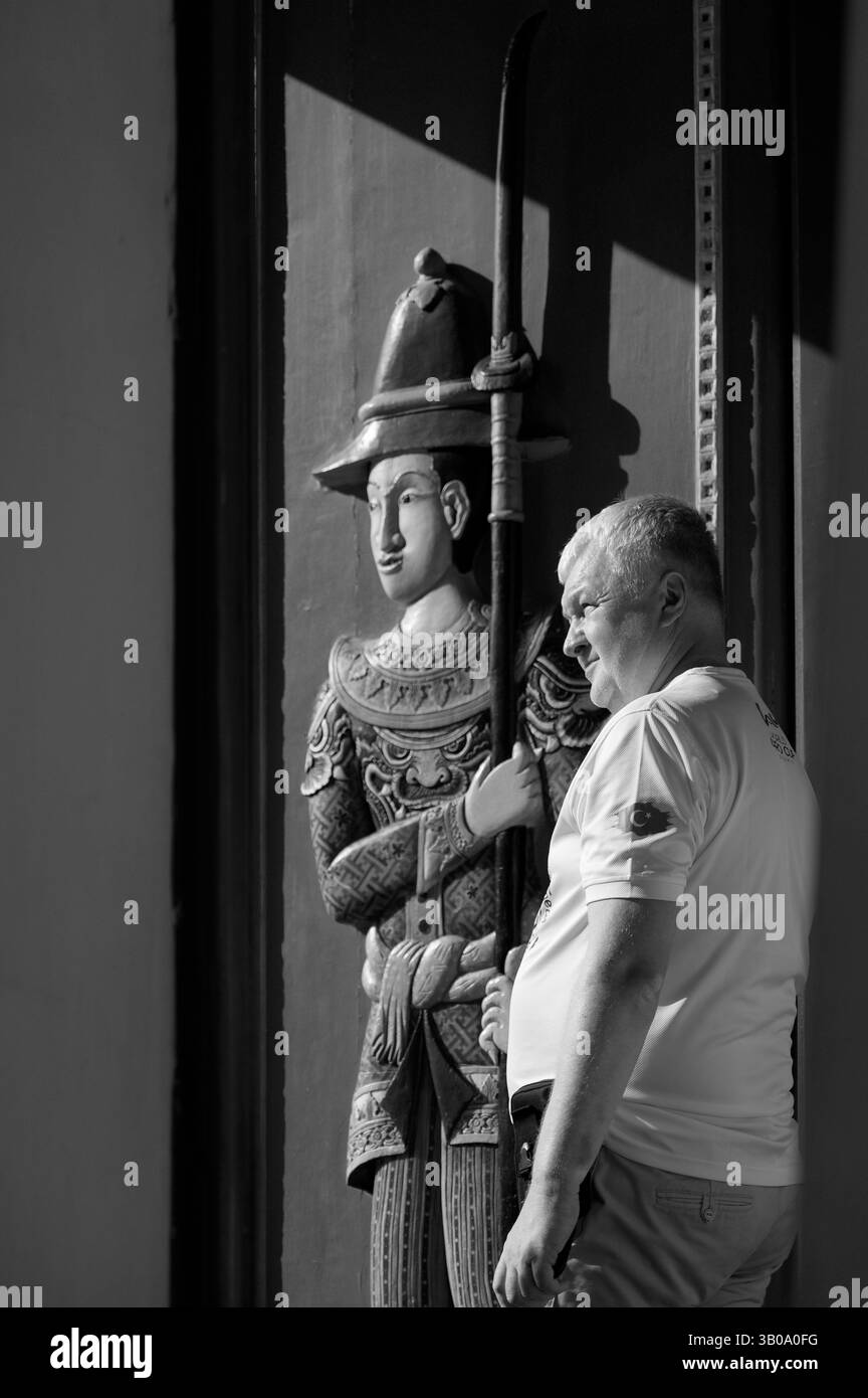 Un visitatore fa una pausa accanto a un tradizionale guardiano scolpito presso il Grand Palace Foto Stock