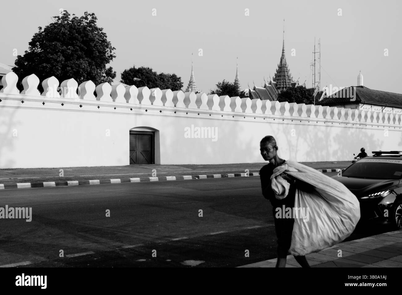 Una figura anziana cammina oltre le grandi pareti bianche del Grand Palace Foto Stock
