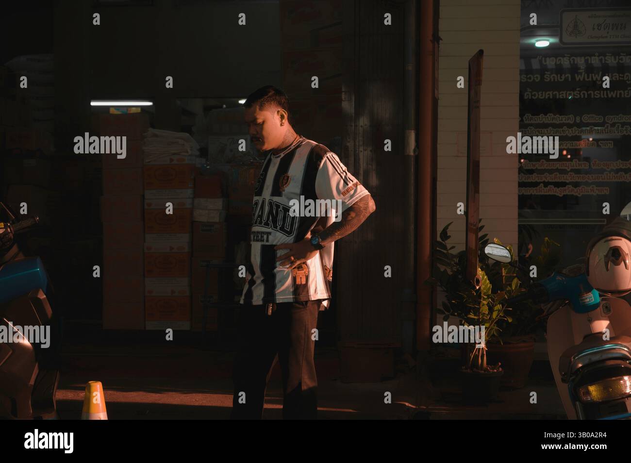 L'uomo si trova in una spettacolare luce serale fuori da un negozio nel centro di Bangkok Foto Stock