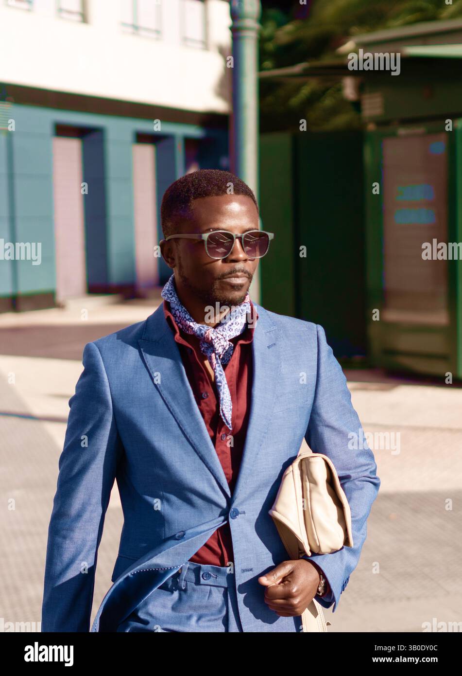 Un Dapper Man vestito con un elegante outfit con occhiali da sole e un accessorio sciarpa Foto Stock