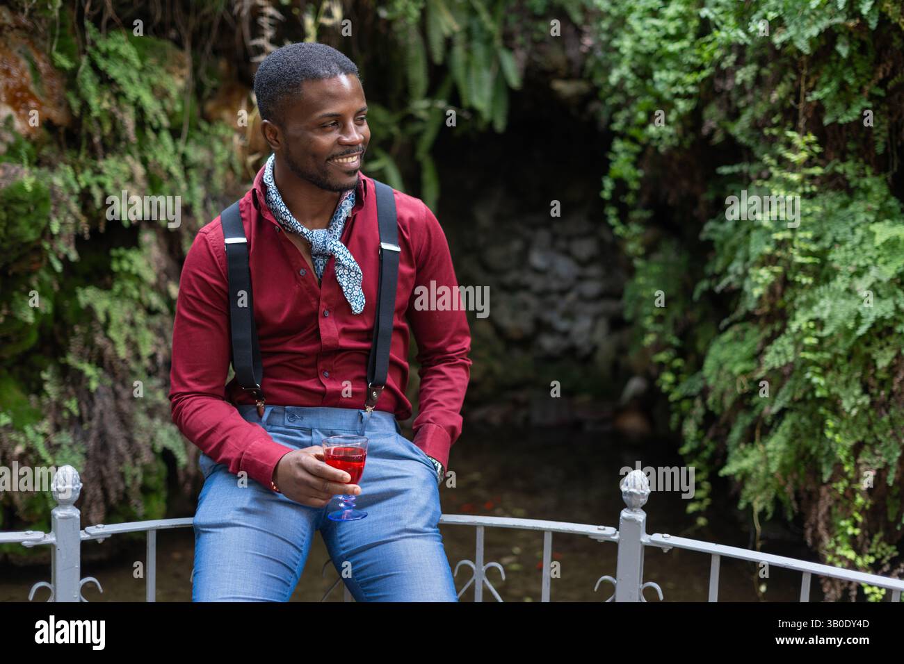 Un uomo elegante che posa nella splendida natura mentre tiene in mano una bevanda rinfrescante Foto Stock