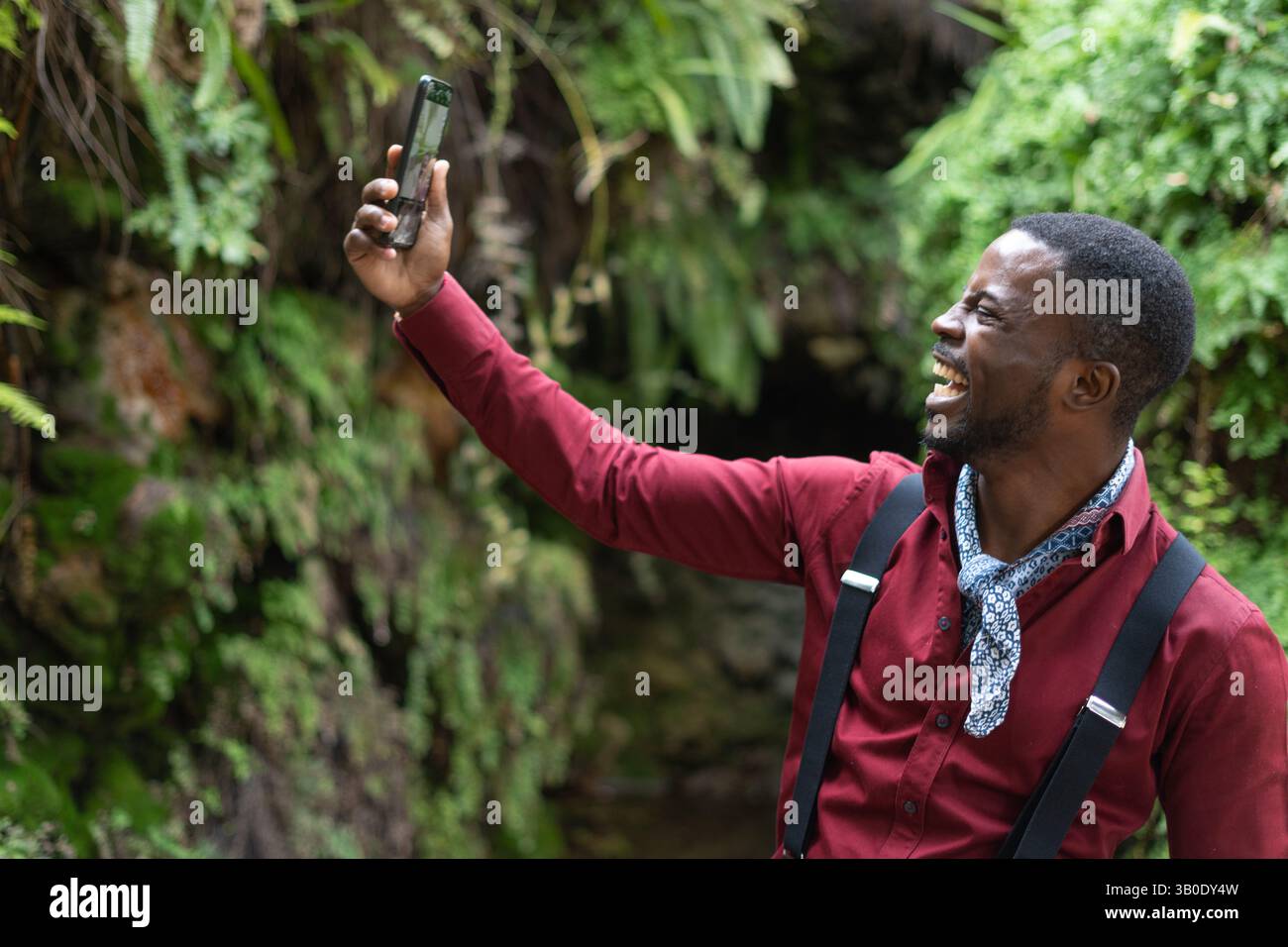 Un uomo che porta felicemente un selfie in un bellissimo e lussureggiante ambiente naturale della sua avventura Foto Stock