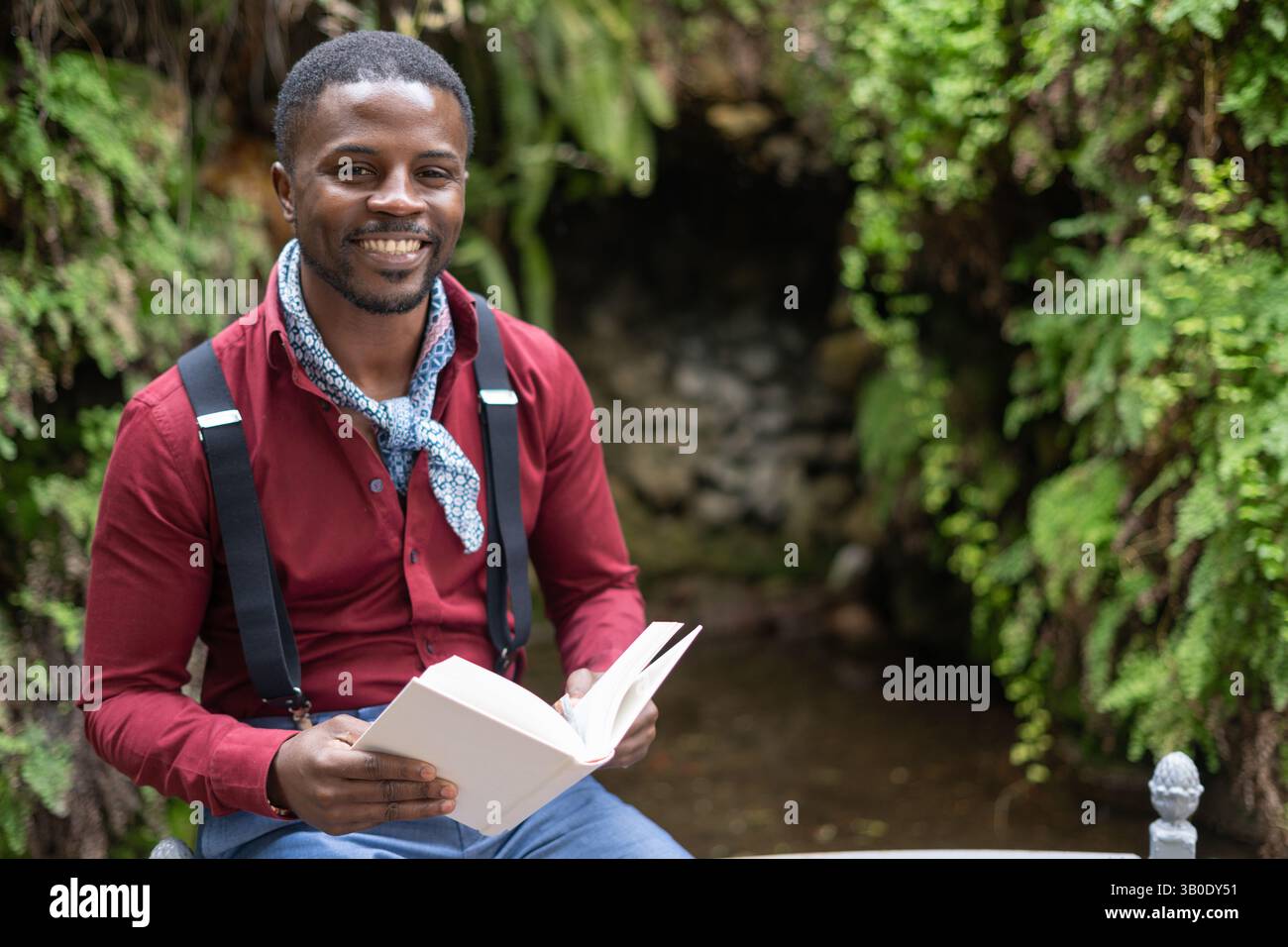 Scrittore sorridente che si diverte a leggere un libro in un giardino tranquillo Foto Stock