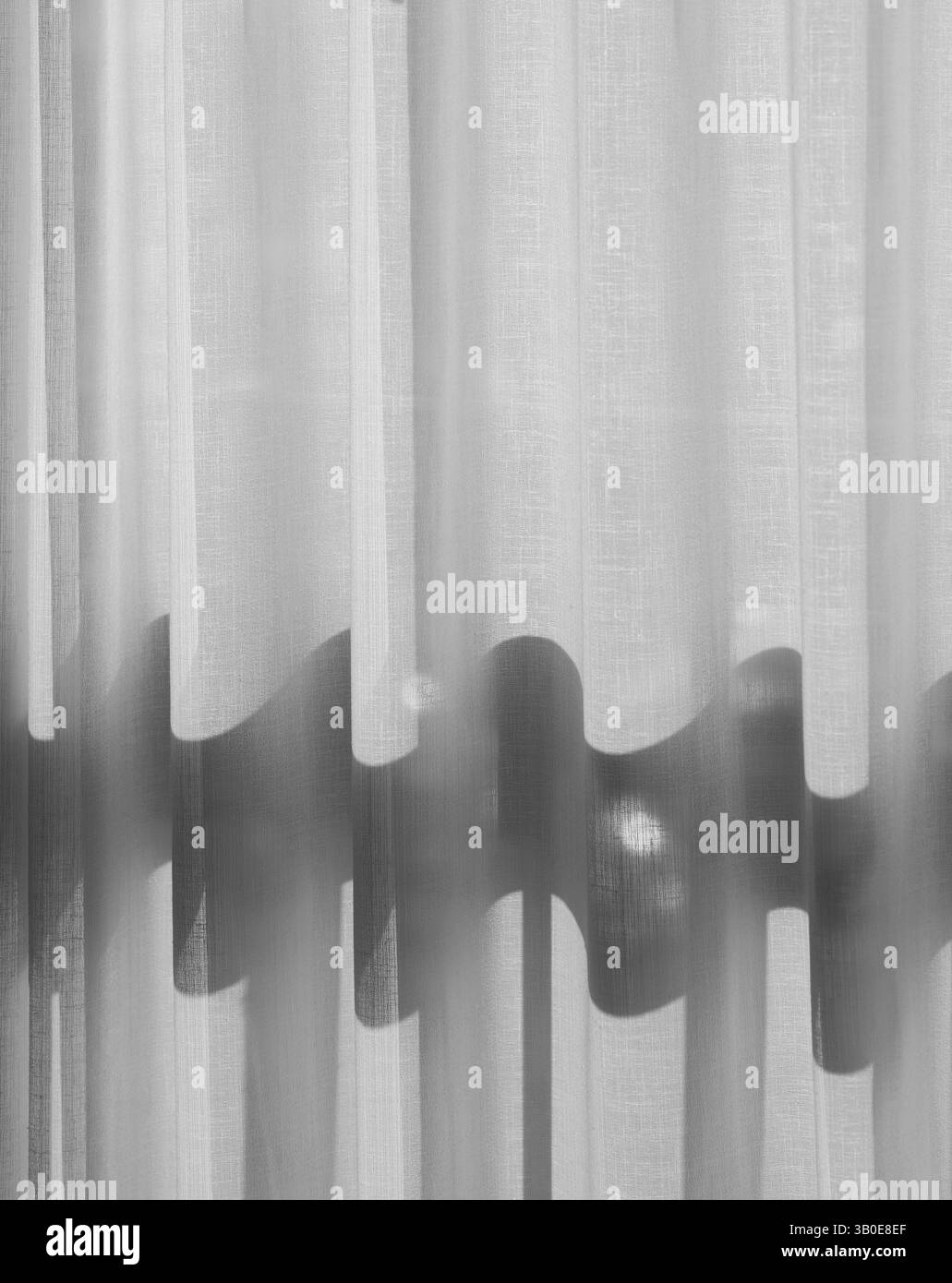 foto in bianco e nero della tenda della finestra in una camera d'albergo con luce che splende creando un'ombra ondulata attraverso il movimento verticale del materiale della tenda Foto Stock foto in bianco e nero della tenda della finestra in una camera d'albergo con luce che splende creando un'ombra ondulata attraverso il movimento verticale del materiale della tenda Foto Stock