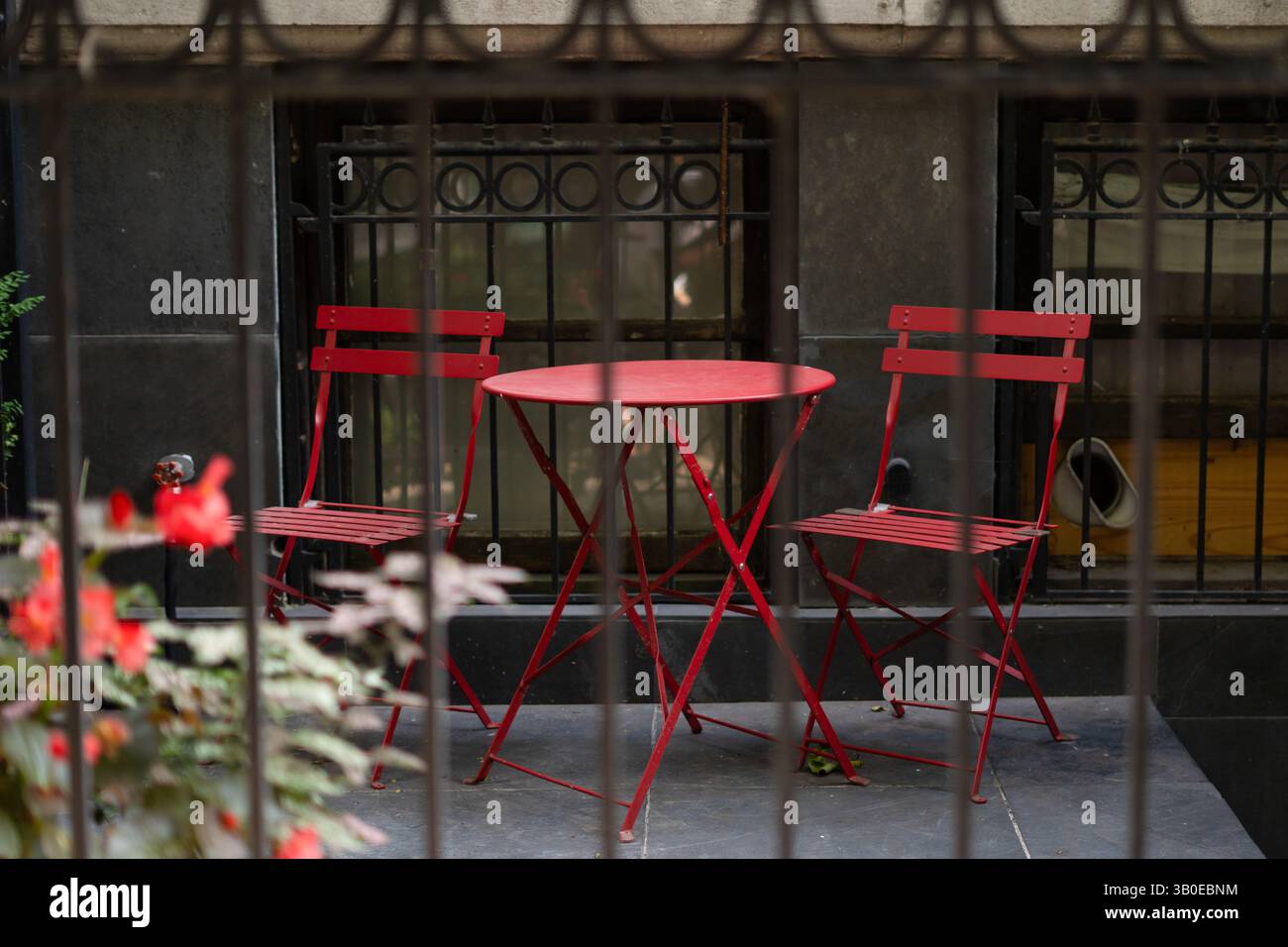 Vivace tavolo rosso con due sedie abbinate in un accogliente patio esterno. Immagine perfetta per cenare, rilassarsi, design urbano, cultura caffè, romantico Foto Stock