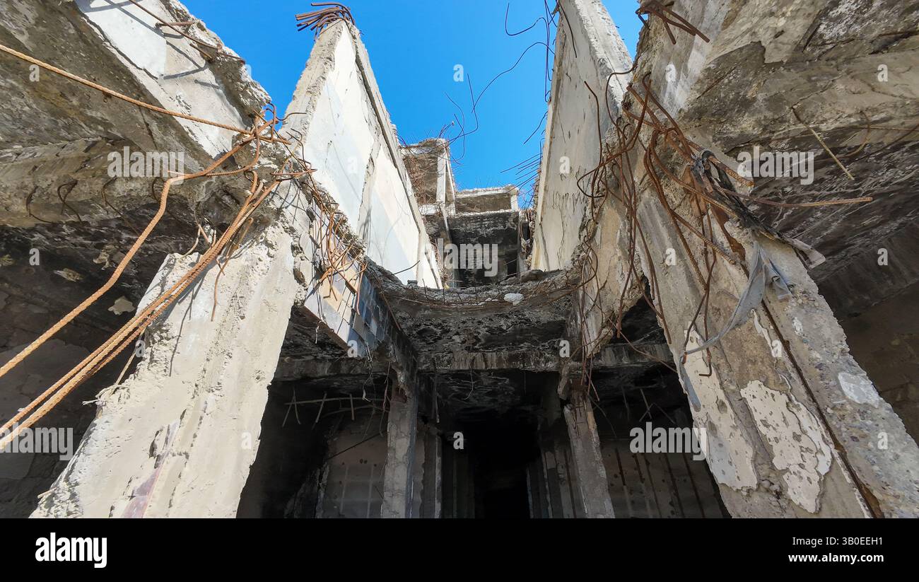Una vista ad angolo basso di un edificio abbandonato e fatiscente con armature esposte e cemento sbriciolato contro un cielo azzurro. Foto Stock