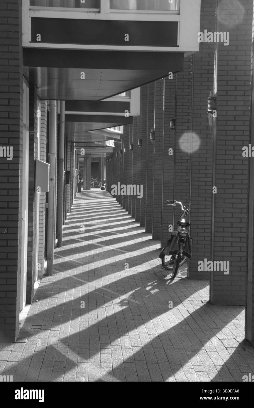 Un vicolo stretto con pareti in mattoni, interrotto da motivi d'ombra. Una bicicletta si inclina contro il muro mentre il vicolo si estende in lontananza. Foto Stock