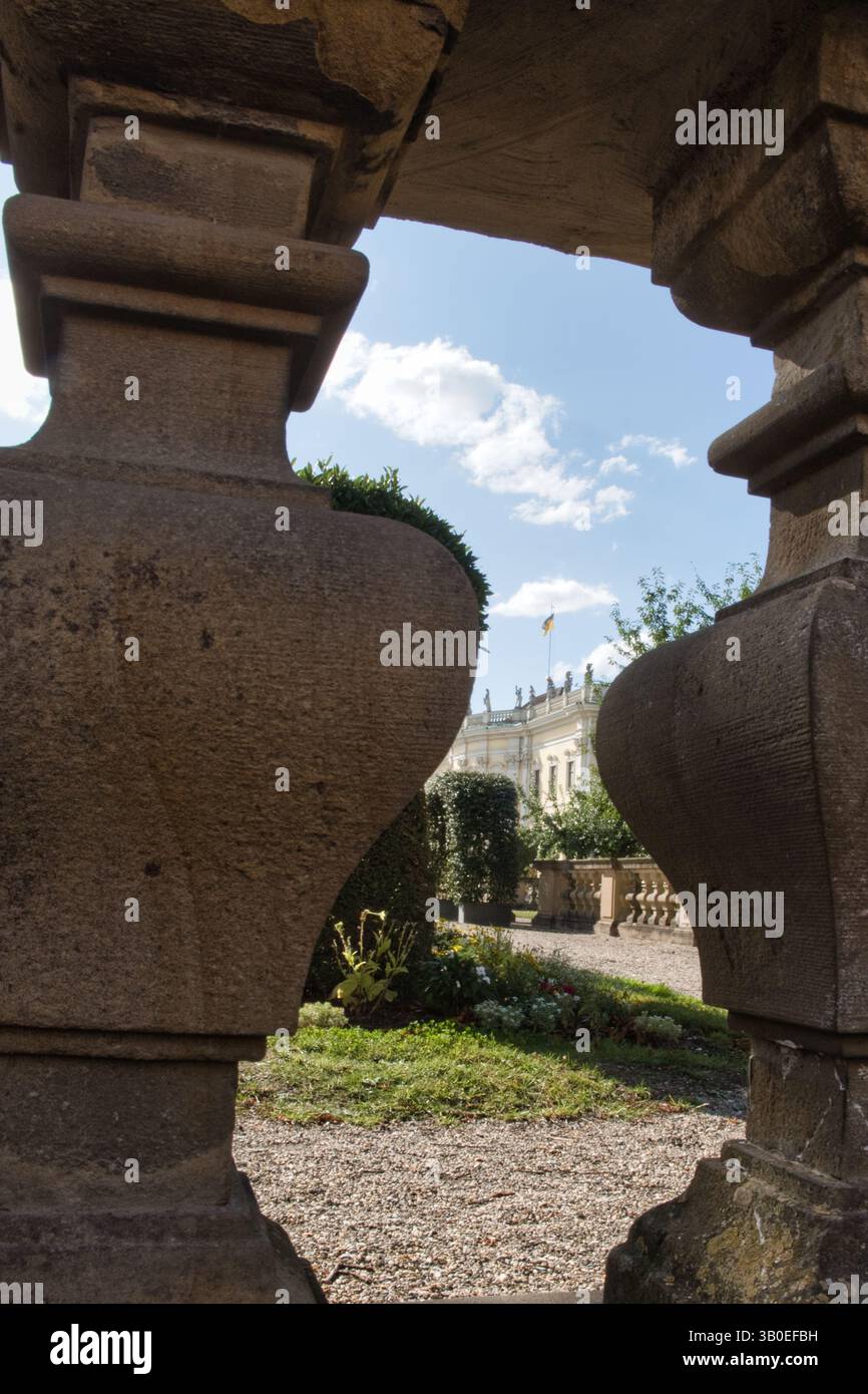 Due grandi balaustre in pietra incorniciano la vista di un giardino verde con un edificio sullo sfondo, mentre il cielo con alcune nuvole completa la scena Foto Stock