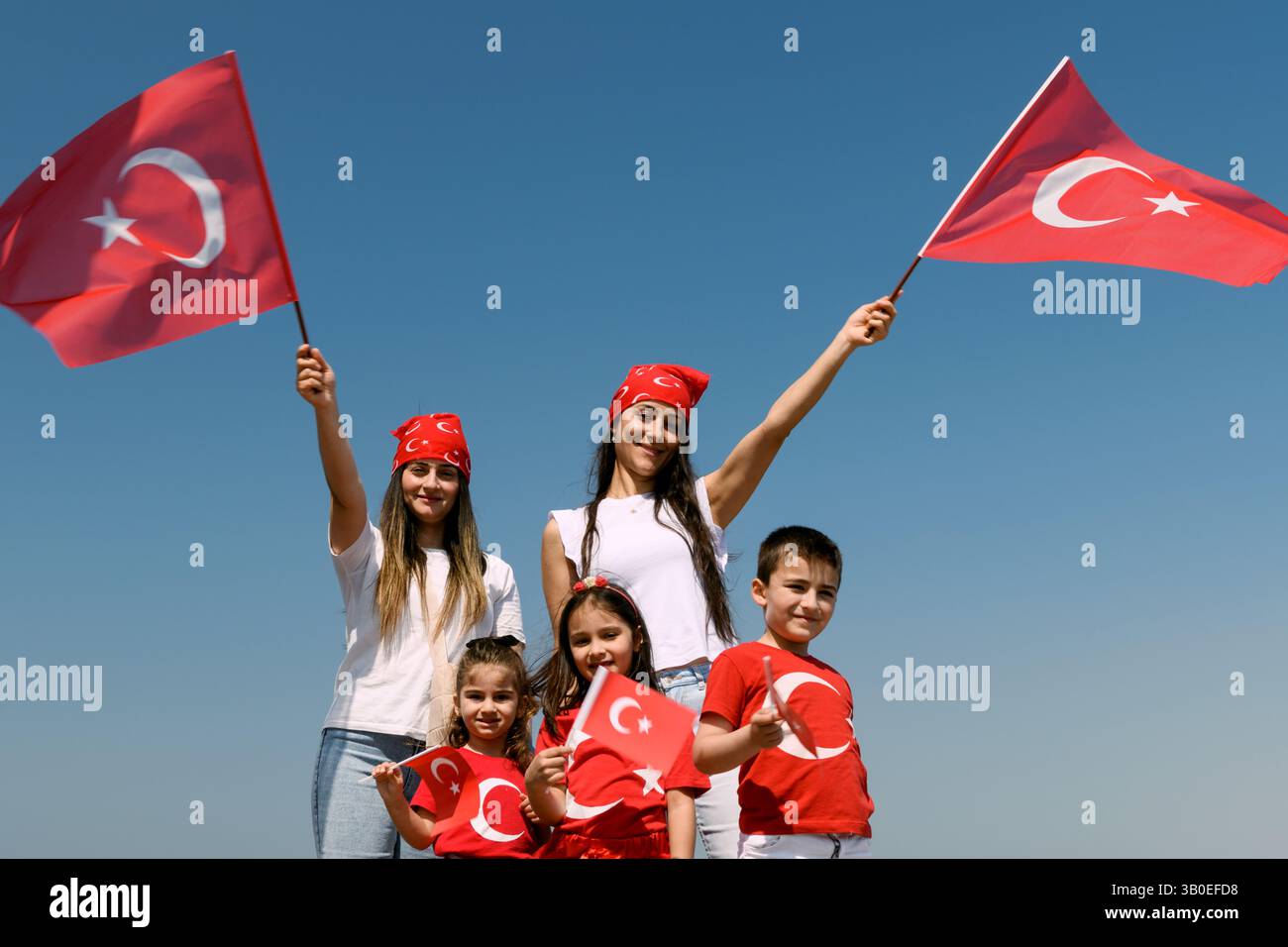 Izmir, Turchia - 23 aprile 2025: Due madri e tre bambini sorridono e ondeggiano le bandiere turche durante le celebrazioni della sovranità nazionale e della giornata dei bambini u Foto Stock