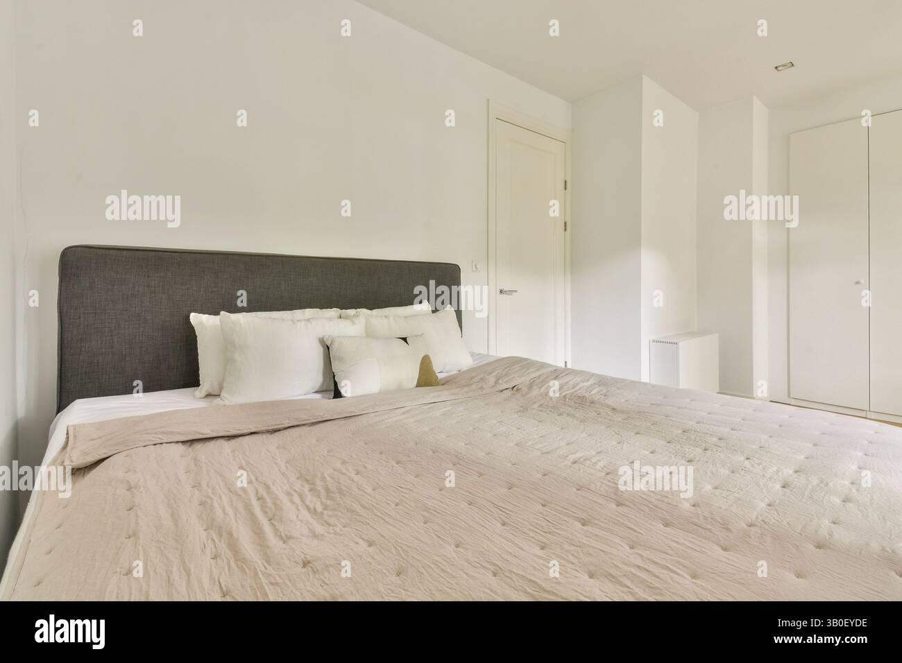 Una camera da letto moderna luminosa e ariosa caratterizzata da una tavolozza di colori neutri con un soffice letto, decor semplice e linee pulite. Ideale per il relax e il comfort. Foto Stock