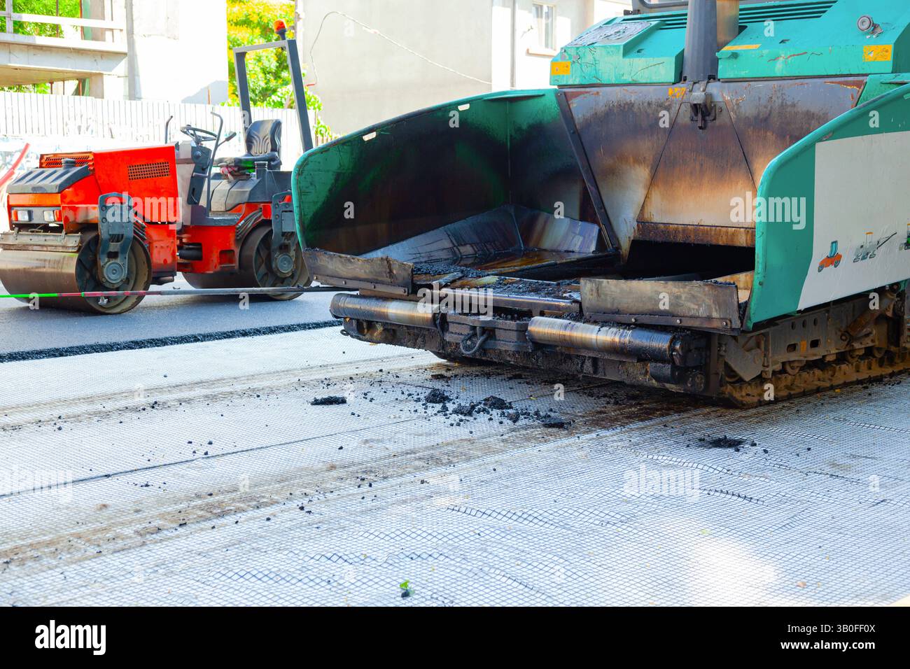 Un'asfaltatrice e un rullo stradale stanno lavorando per stendere nuovo asfalto sulla strada. Foto Stock
