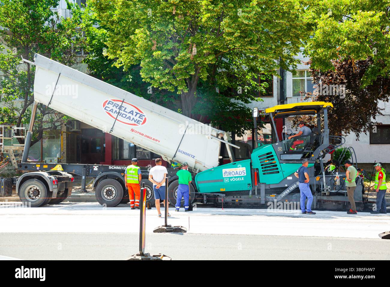 I lavoratori stanno lavorando alla riparazione della strada e un'asfaltatrice sta lavorando alla posa di nuovo asfalto sulla strada. Foto Stock