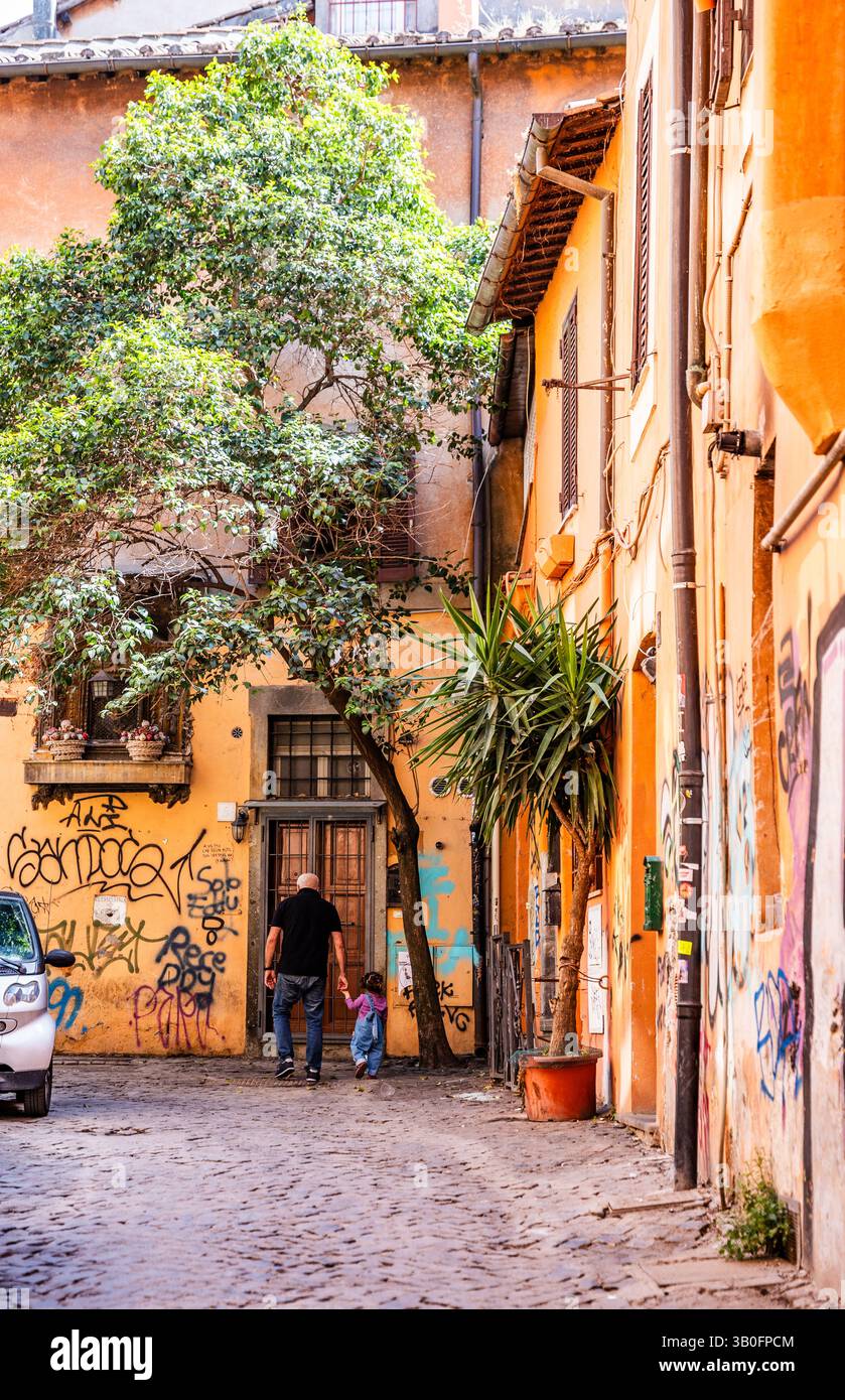 Scorcio di un vicolo tranquillo con case residenziali coperte di edera e vegetazione lussureggiante, nonno e nipote, nel quartiere Trastevere, a Roma, Italia. Foto Stock
