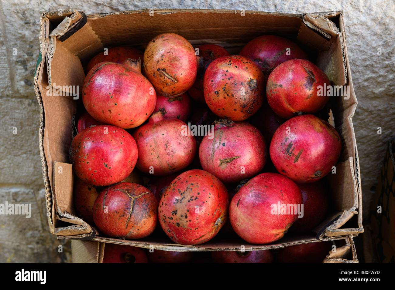 Una scatola di cartone di frutta rossa e matura di melograno in una bancarella di succhi di frutta in un mercato israeliano. Foto Stock