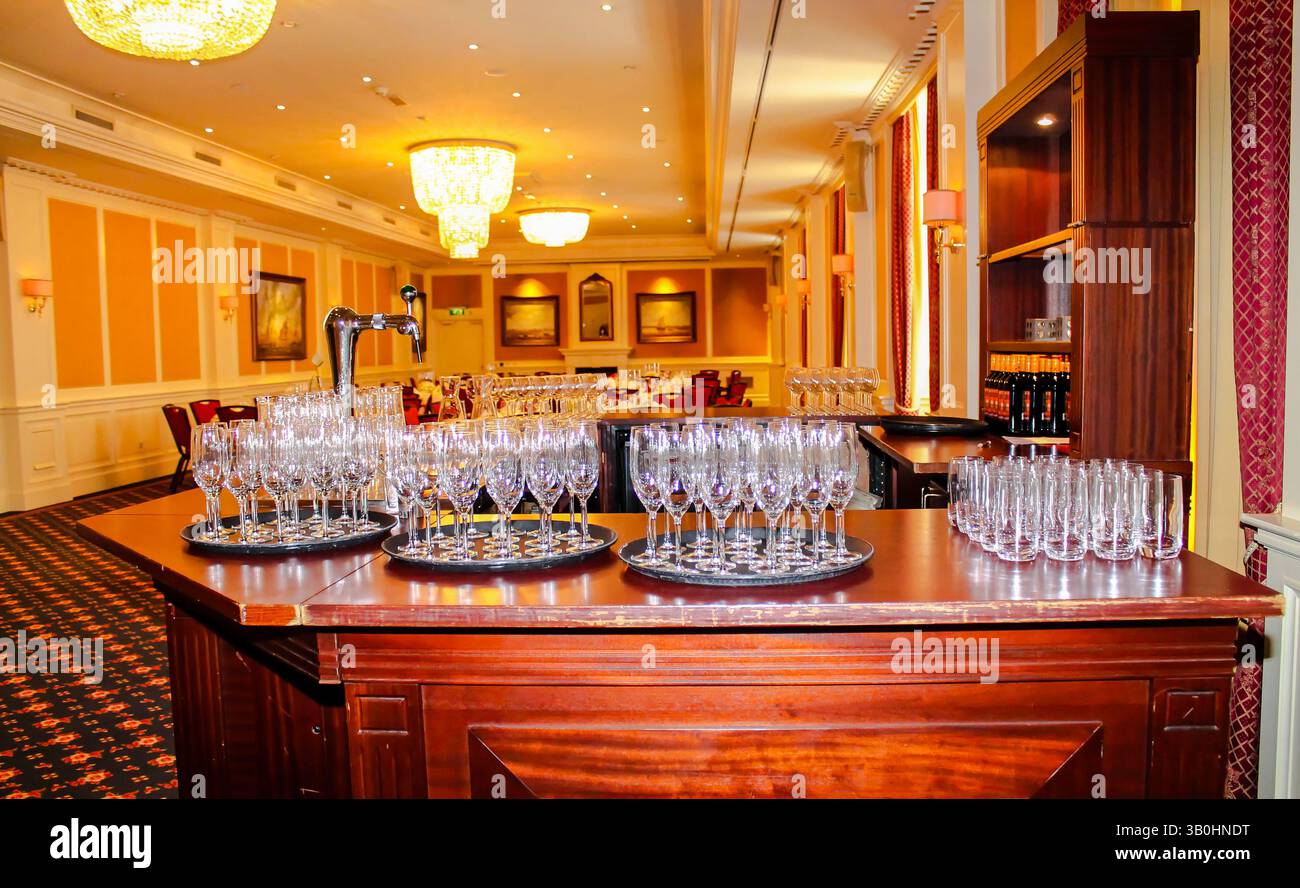 Un'area bar splendidamente arredata in una sala banchetti, con vassoi multipli di bicchieri da vino frizzante pulito. Il decor elegante include lampadari e Foto Stock