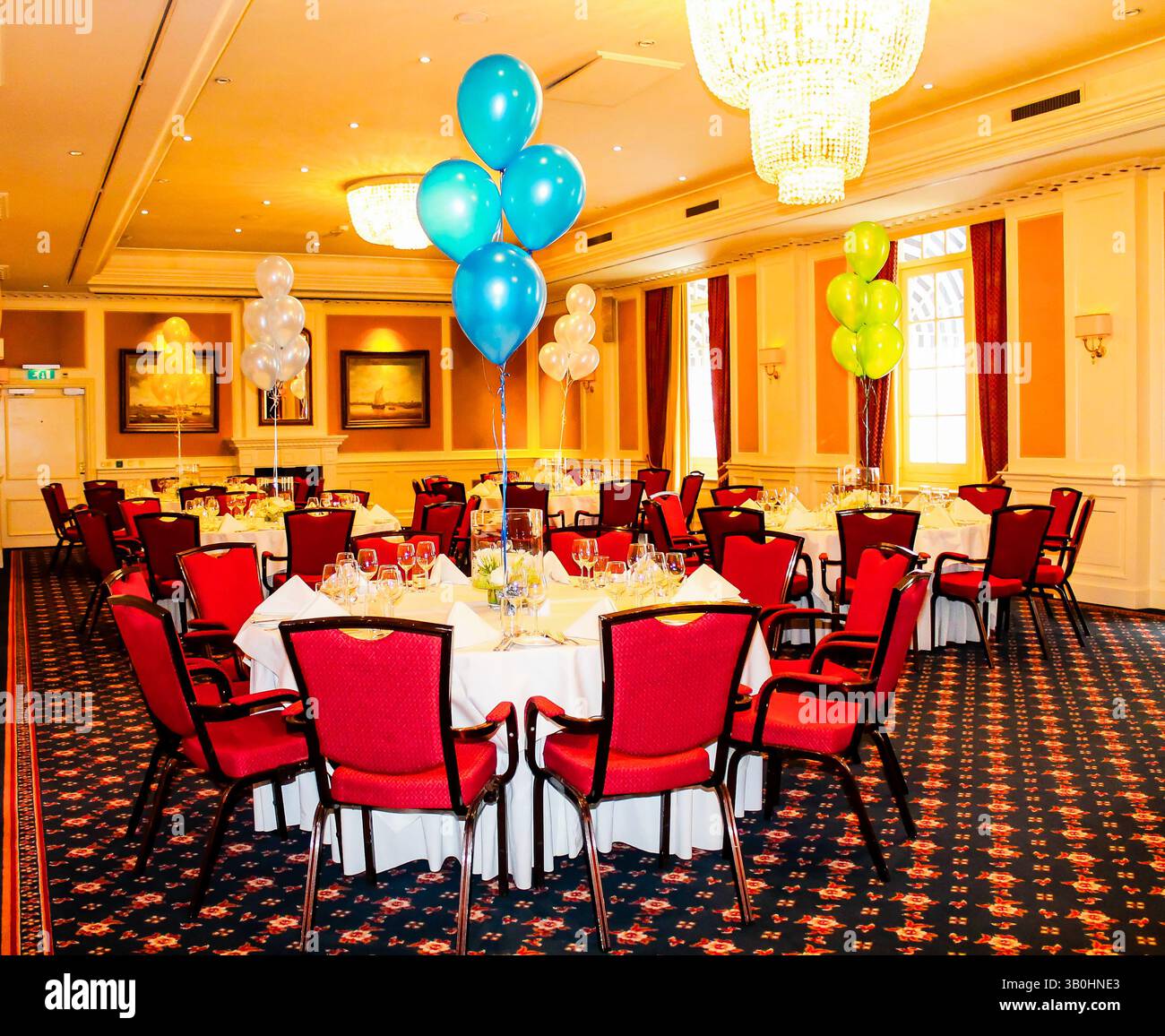 Elegante sala banchetti con tavoli rotondi, sedie rosse e palloncini colorati. Foto Stock