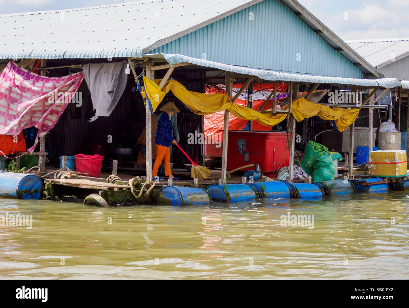 Una donna spazza il pavimento del suo negozio galleggiante sul fiume Mekong, Tan Chau, Vietnam Foto Stock