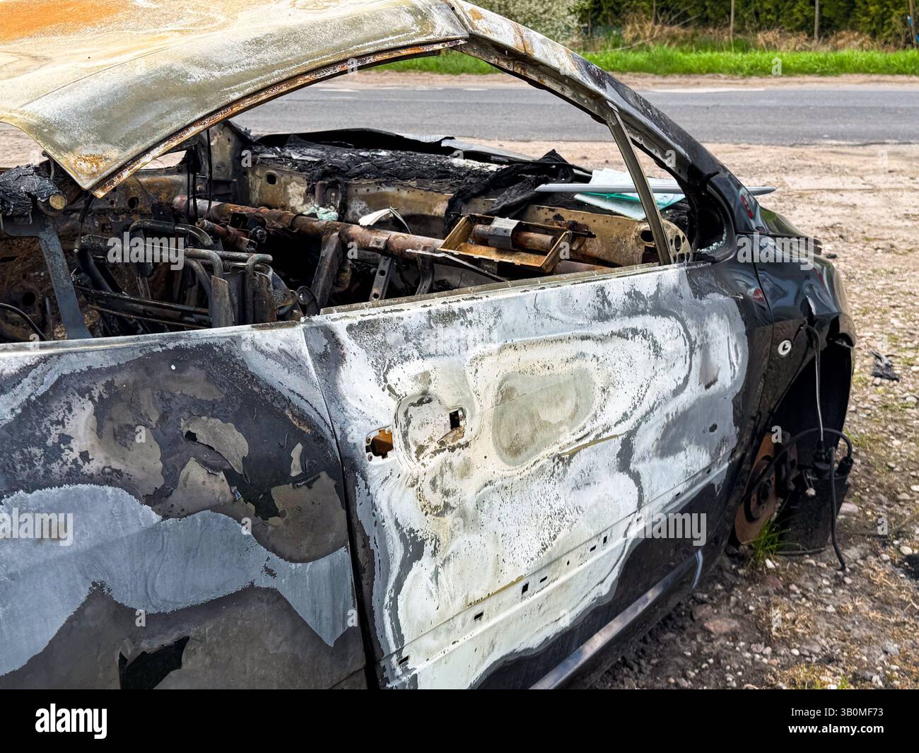 Vista laterale di un'auto completamente bruciata che mostra vernice deformata e blister, interni mancanti e componenti arrugginiti dopo un intenso incendio in prossimità di Foto Stock