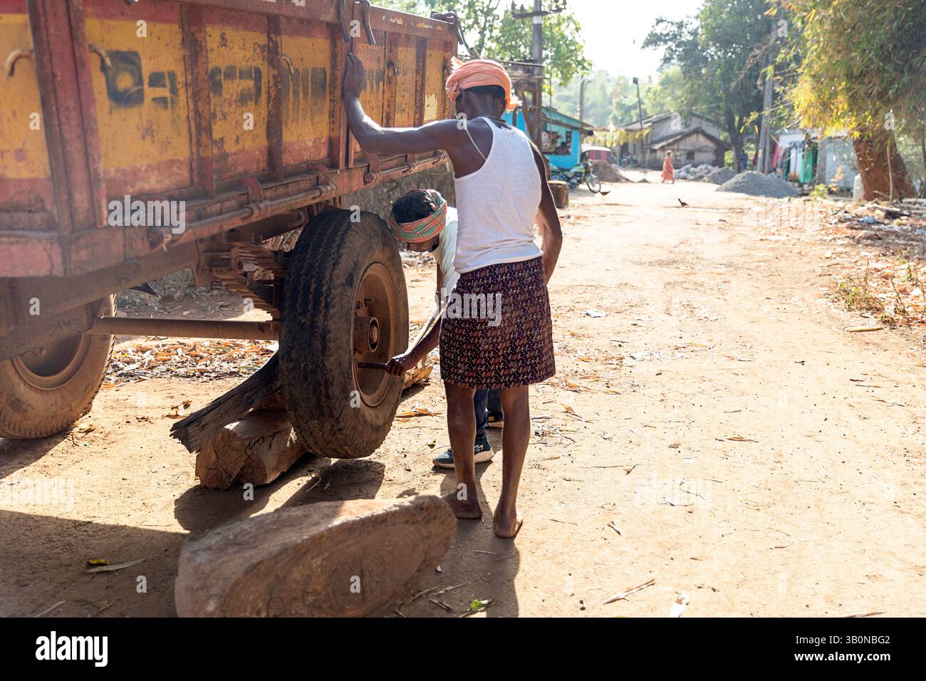Uomini del posto che cambiano una gomma su un vecchio rimorchio in un piccolo villaggio di orissa, india Foto Stock