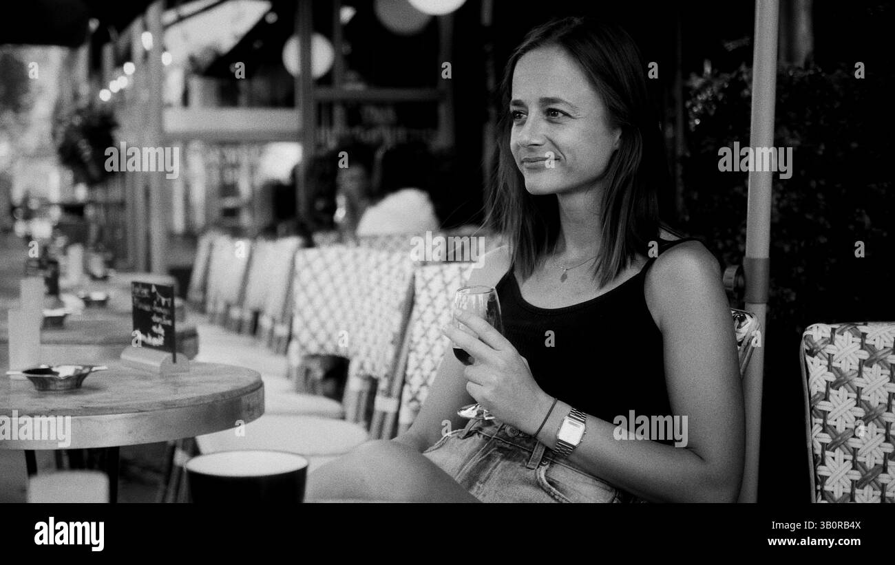 Giovane donna che si gusta un bicchiere di vino in un caffè parigino Foto Stock