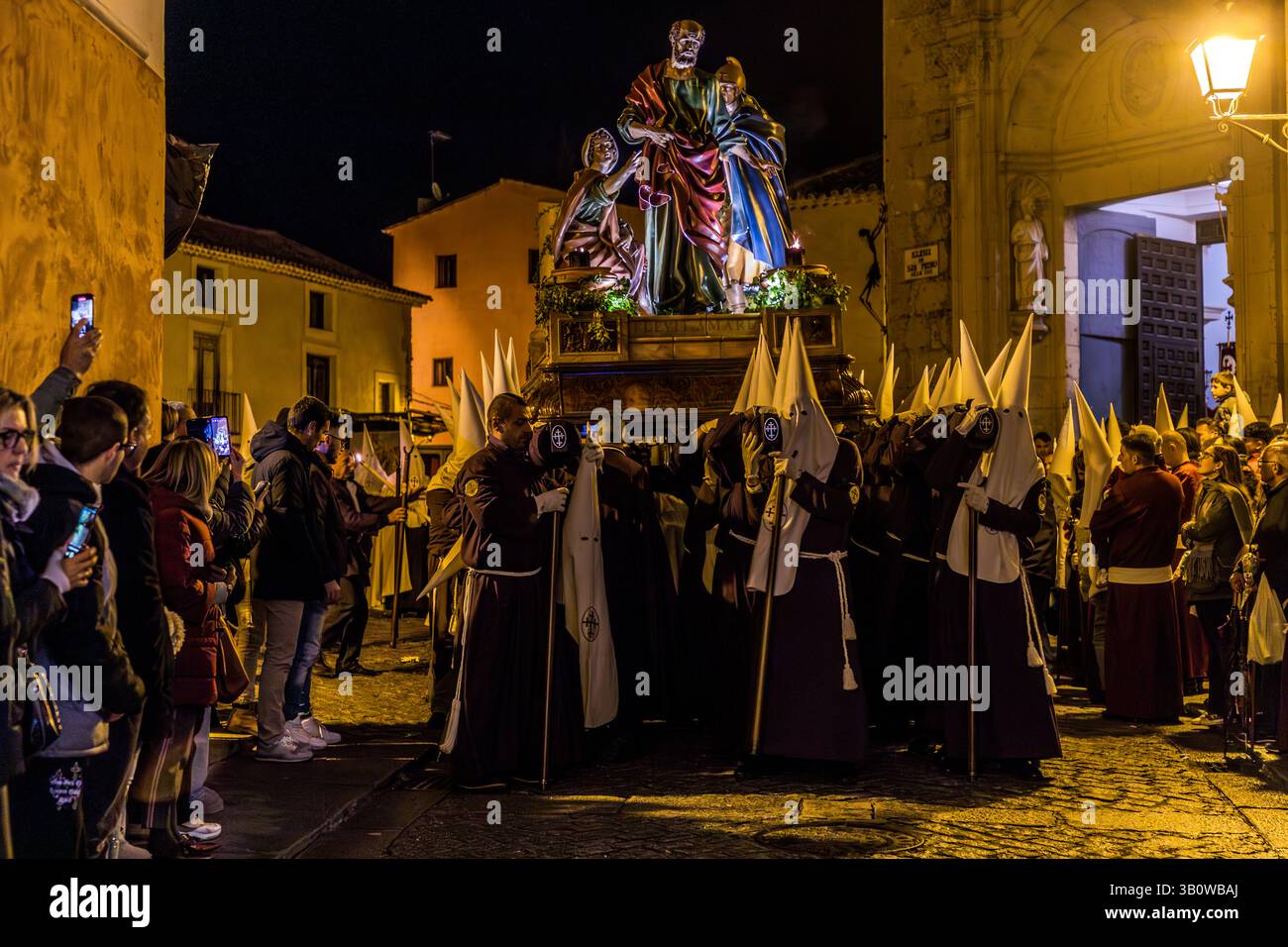 Processione in Spagna di notte con figure religiose su un galleggiante e molti partecipanti ai costumi processuali dell'Hermandad de la Negatión de San Pedro. Pietro è raffigurato sul paso negando di conoscere Gesù. Calle Trabuco, Cuenca, Castilla-la Mancha, Spagna Foto Stock