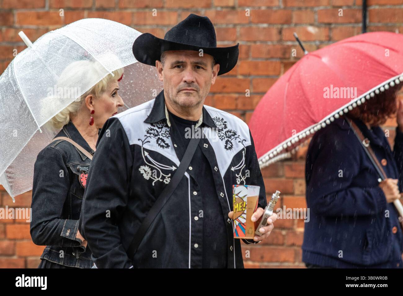 Al Maverick americana Music Festival del 2019 a Easton Farm Park Suffolk, un frequentatore del festival con cappello e camicia da cowboy tiene un bicchiere di birra e uno svapo. Foto Stock