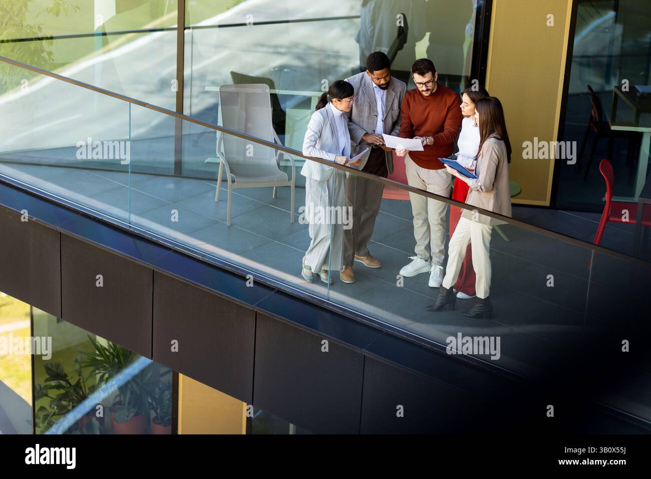 Quattro professionisti si riuniscono su un balcone, discutendo dei progetti mentre si godono la luce del sole. Foto Stock