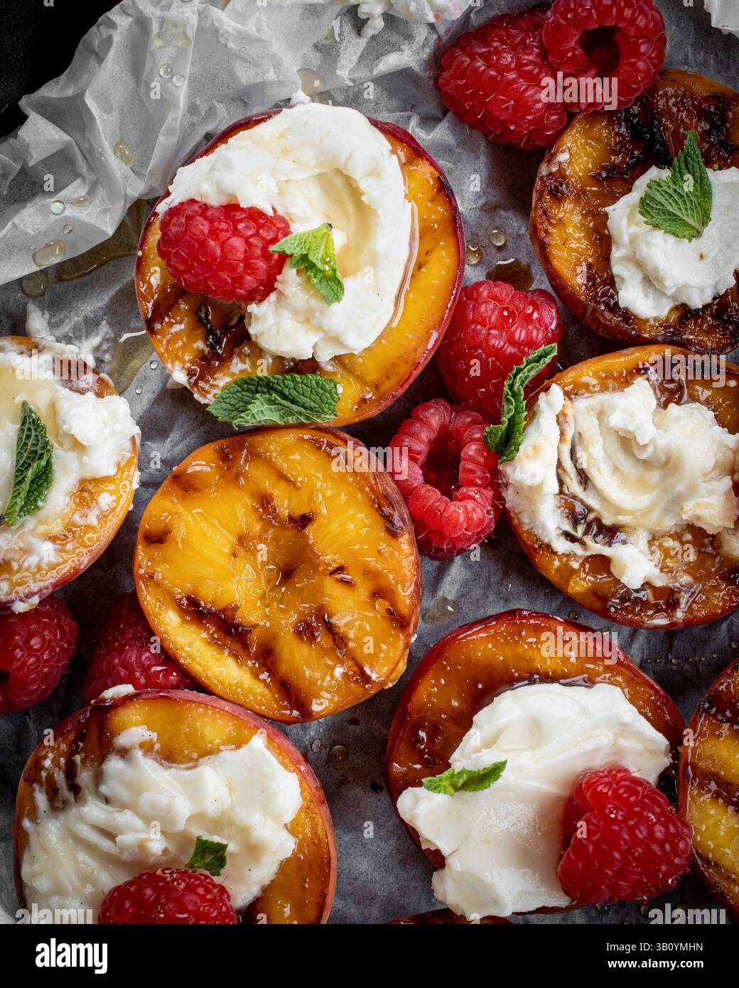 Pesche grigliate ricoperte di mascarpone ai chicchi di vaniglia e servite con lamponi e miele Foto Stock