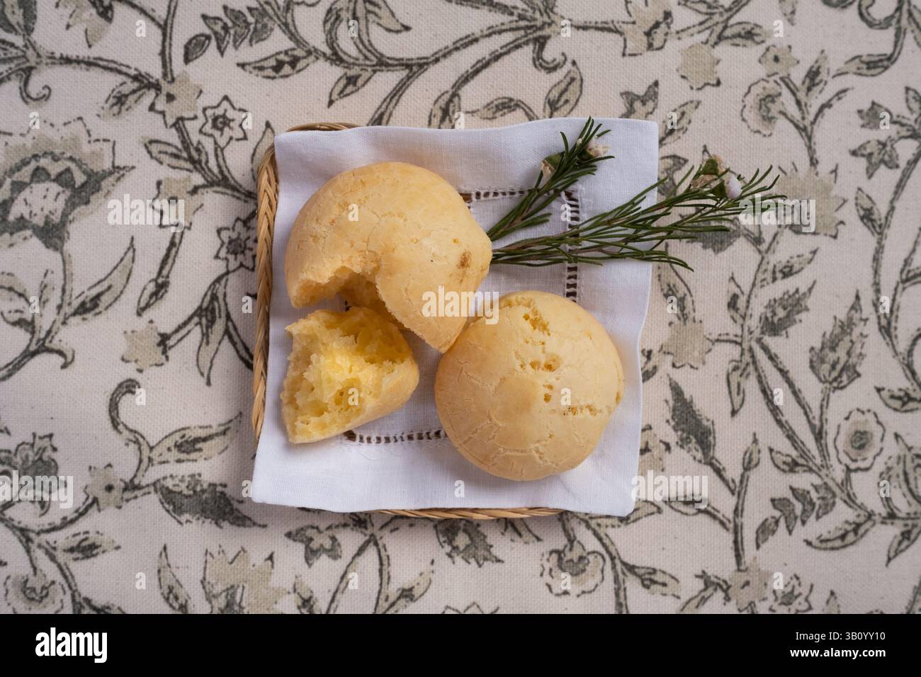 Piccolo vassoio di vimini con due tipi di pane al formaggio tradizionali provenienti dal Brasile e dal Portogallo, guarniti con un rametto di rosmarino. Sono freschi, cotti e fatti a mano. Foto Stock
