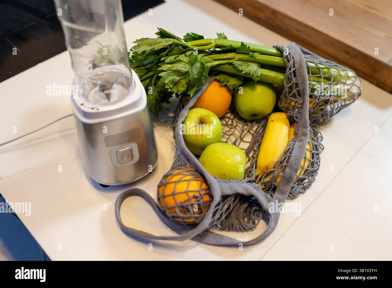 Borsa in rete accanto al frullatore personale su un piano di appoggio bianco, che contiene mele e banane Foto Stock