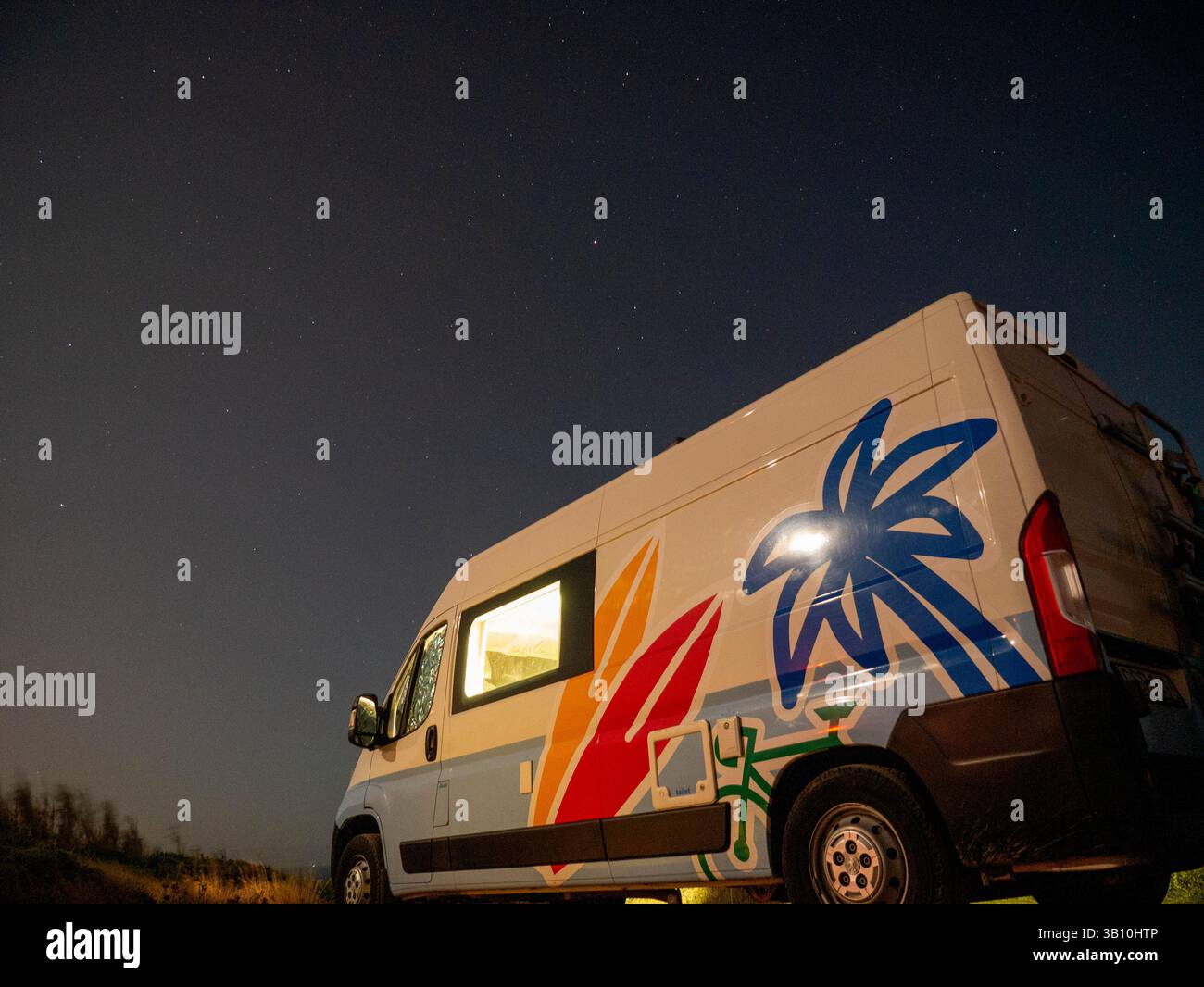 Un vibrante camper con opere d'arte tropicali si trova tranquillamente sotto un cielo stellato in un tranquillo ambiente naturale. Immersa nella luce soffusa della luna, questa camera serena è vicina Foto Stock