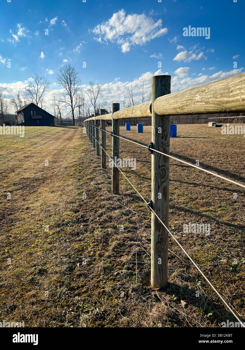 Recinzione in legno per pascoli che conduce attraverso il campo rurale verso il fienile sotto il cielo blu Foto Stock
