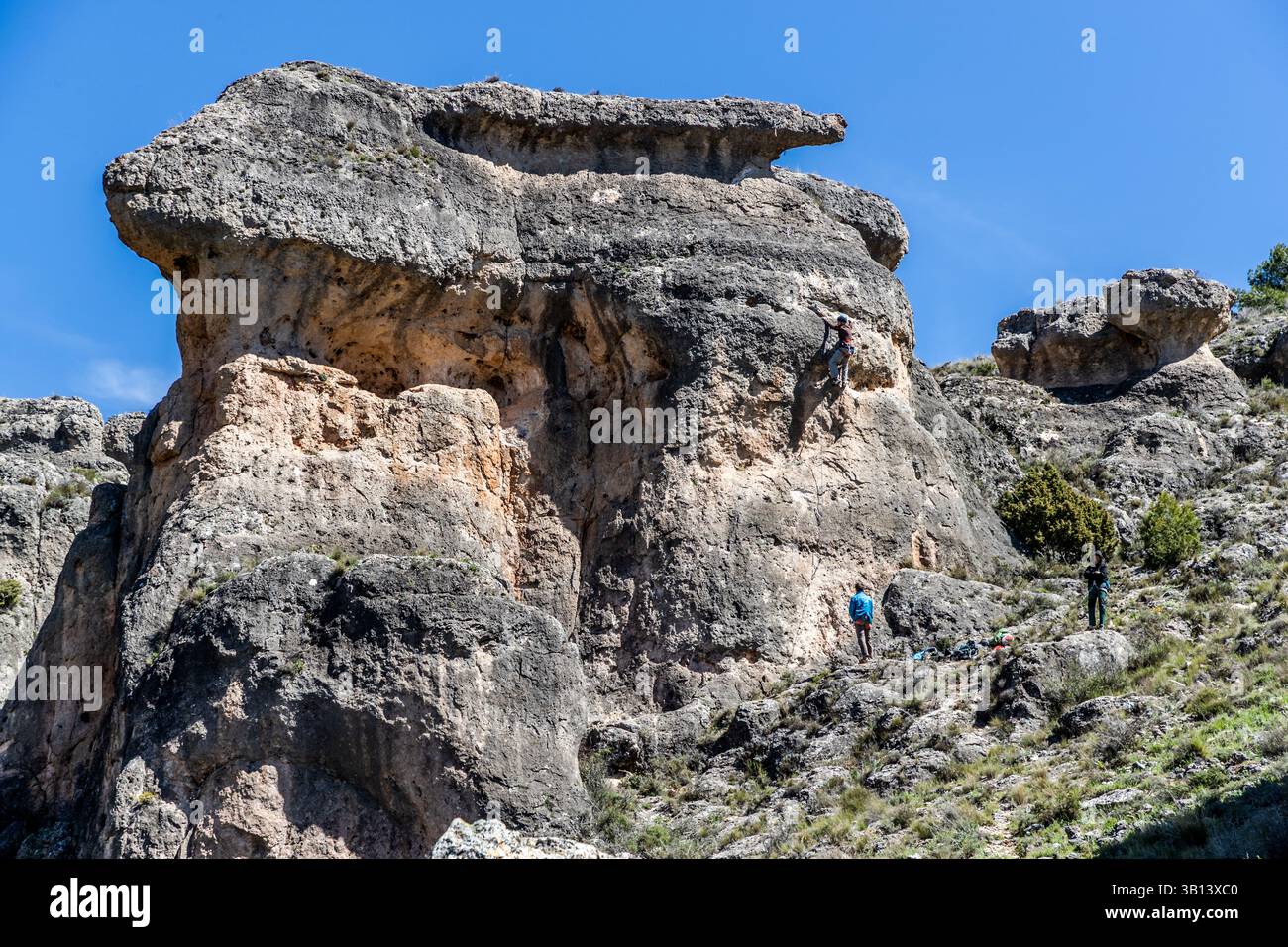 Un arrampicatore scalda una suggestiva formazione rocciosa che assomiglia a un coniglio sul Camino de San Isidro vicino a Cuenca, Castilla-La Mancha, Spagna. Altre due persone assicurano e osservano dai piedi della roccia. Foto Stock