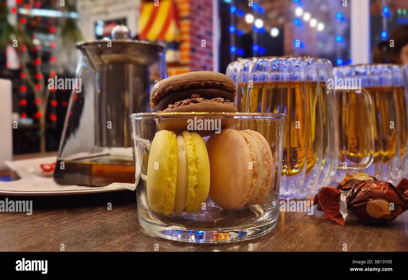 Primo piano di un bicchiere con gustosi macaron, biscotti e tazze da tè sul tavolo all'interno di un elegante e accogliente caffè Foto Stock